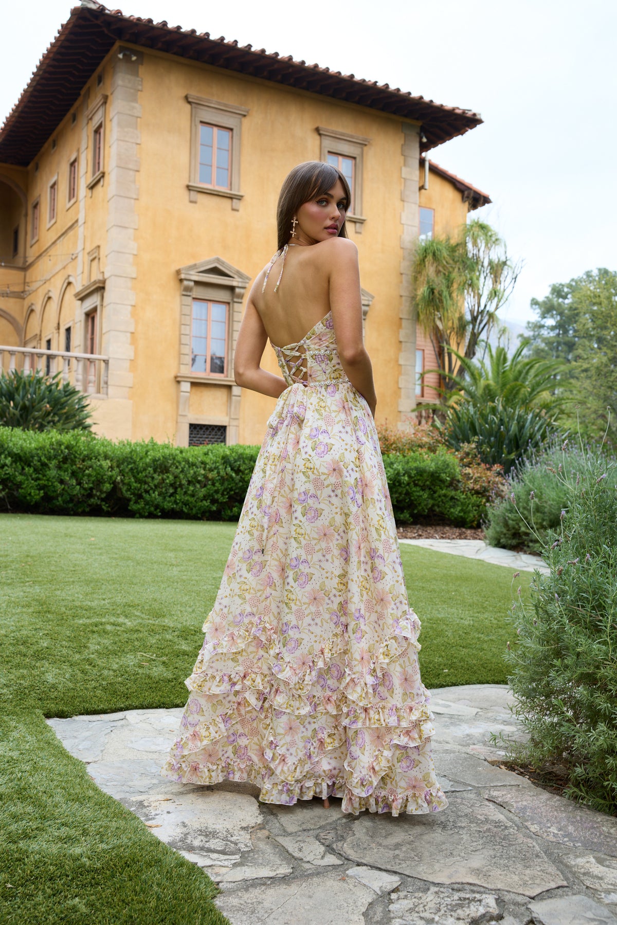 Back view of The Scarlette Dress in Cordoba Print showcasing its lace-up back and ruffled cream floral skirt in a garden