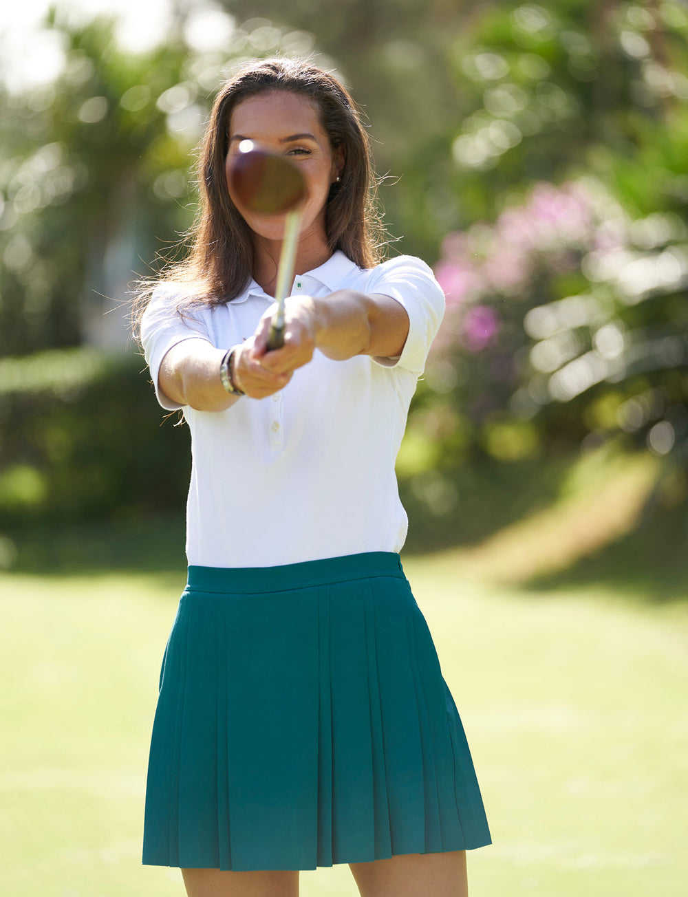 Front view of Langley skirt in teal showcasing pleated A-line silhouette and high waist with a model standing on a sunny golf course