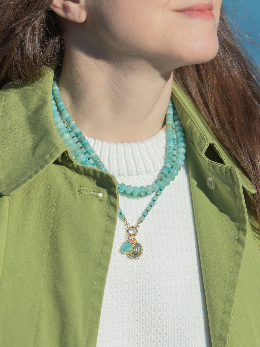 Close-up of model wearing Shay Necklace in blue and green showcasing layered amazonite and turquoise beads with freshwater pearl charm and gold accents against a white sweater and green jacket