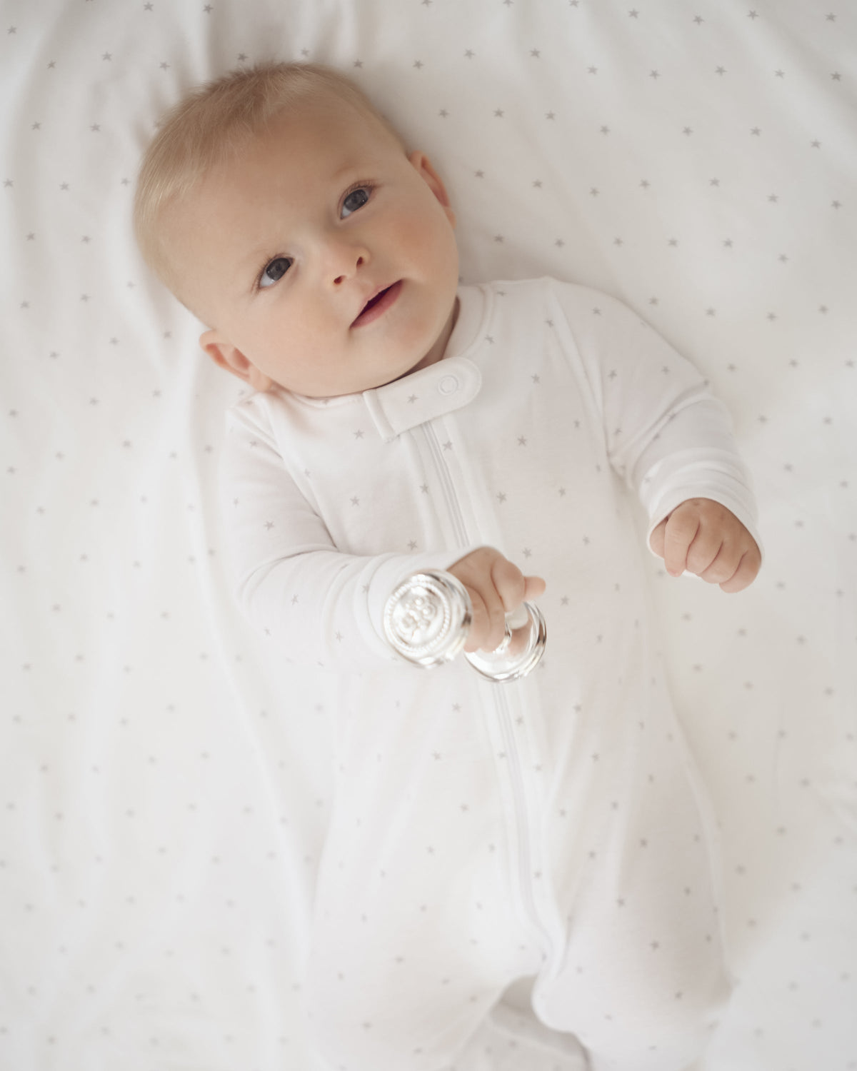 Baby lying on a grey star-patterned Pima cotton blanket and holding a rattle