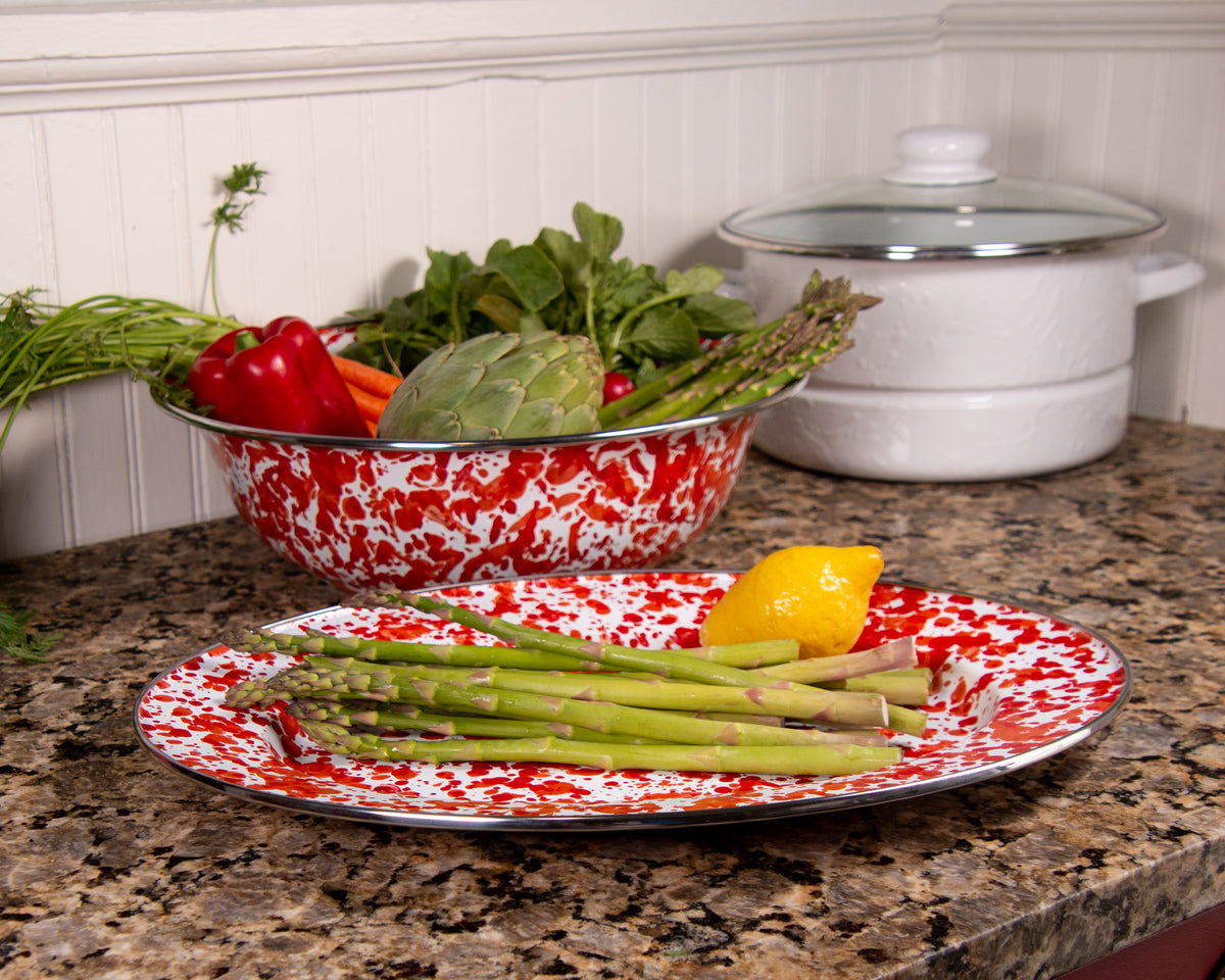 Angled view of Oval Platter in Red Swirl showcasing its red and white enamel pattern with asparagus and lemon on a kitchen counter