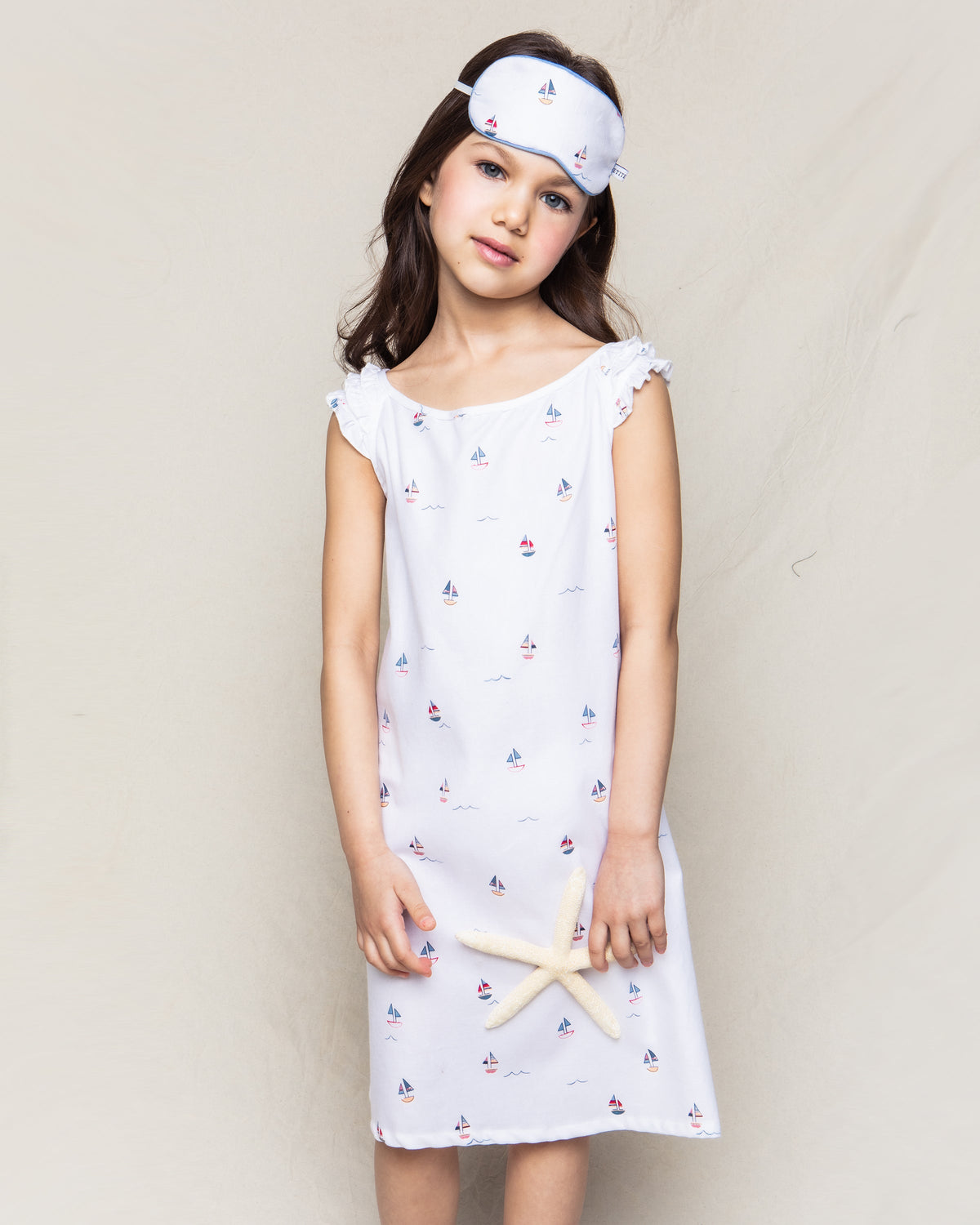 Front view of Amelie nightgown on girl model showing white cotton with small sailboat print, ruffle shoulders, knee-length