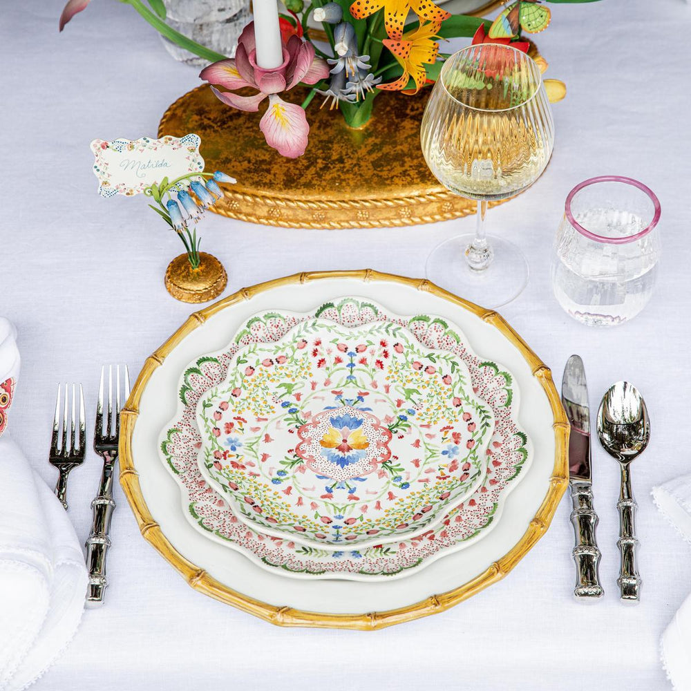 Top-down view of Sofia dessert/salad plate showcasing ruffled scalloped rim and multicolor floral motif on a white tablecloth with gold charger and glassware