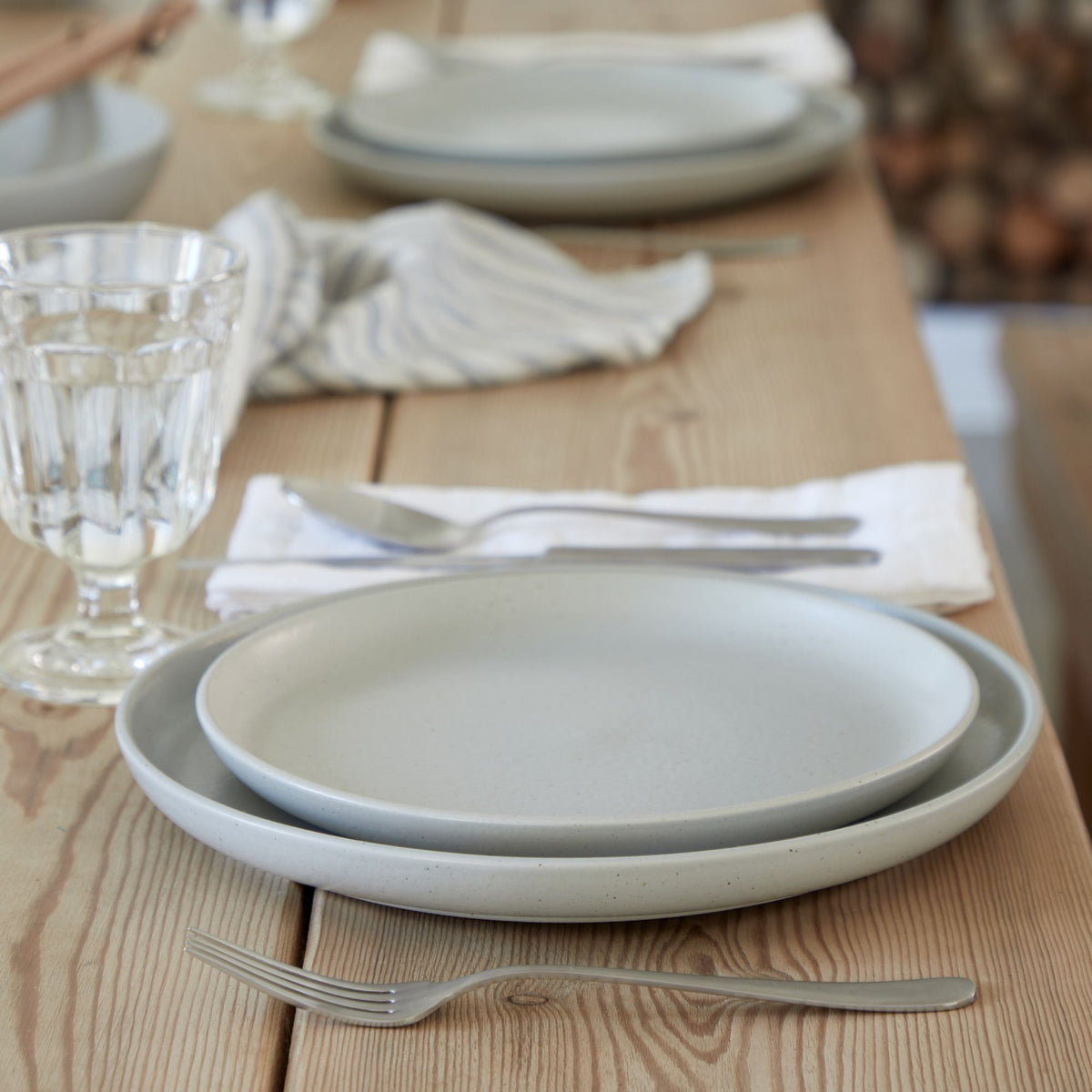 Close-up front view of Pacifica salad plate in oyster grey stacked on a matching dinner plate showing matte glaze on a wooden table
