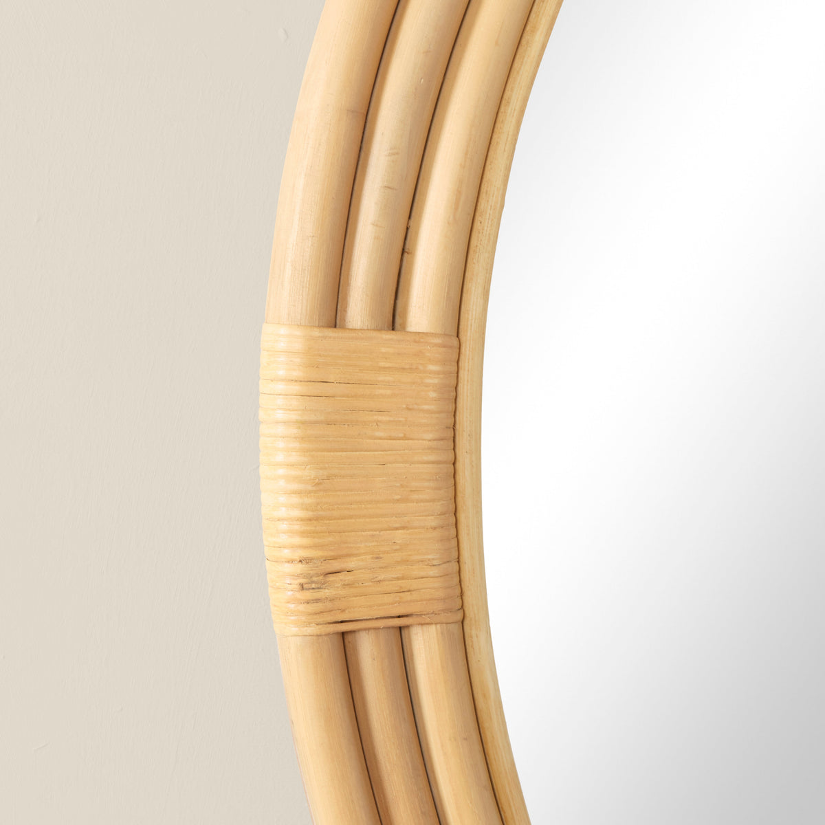 Close-up of Pelicano Small Round Mirror showcasing woven rattan frame and wrapped joint against a light neutral wall