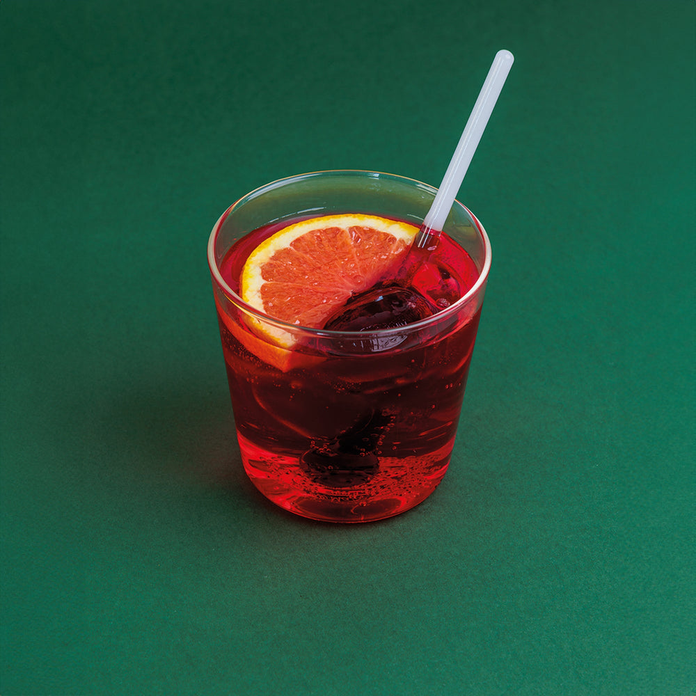 Front view of Spritzometro tumbler filled with red spritz, ice, grapefruit slice and clear stirrer on green background