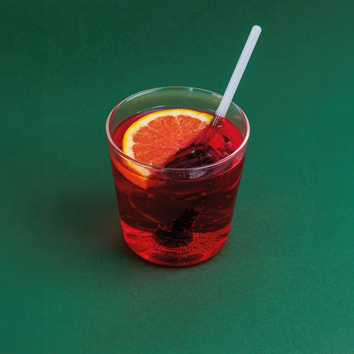 Front view of Spritzometro tumbler filled with red spritz, ice, grapefruit slice and clear stirrer on green background