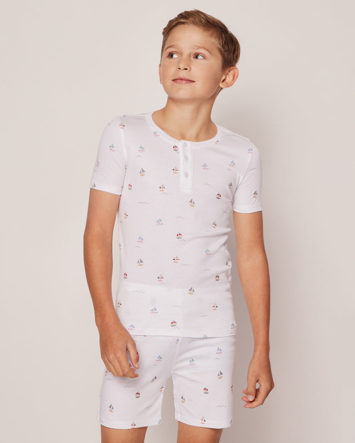 Front view of Pima snug-fit kids’ short pajama set in Bateau showing white henley top and matching shorts with small sailboat print on neutral beige background