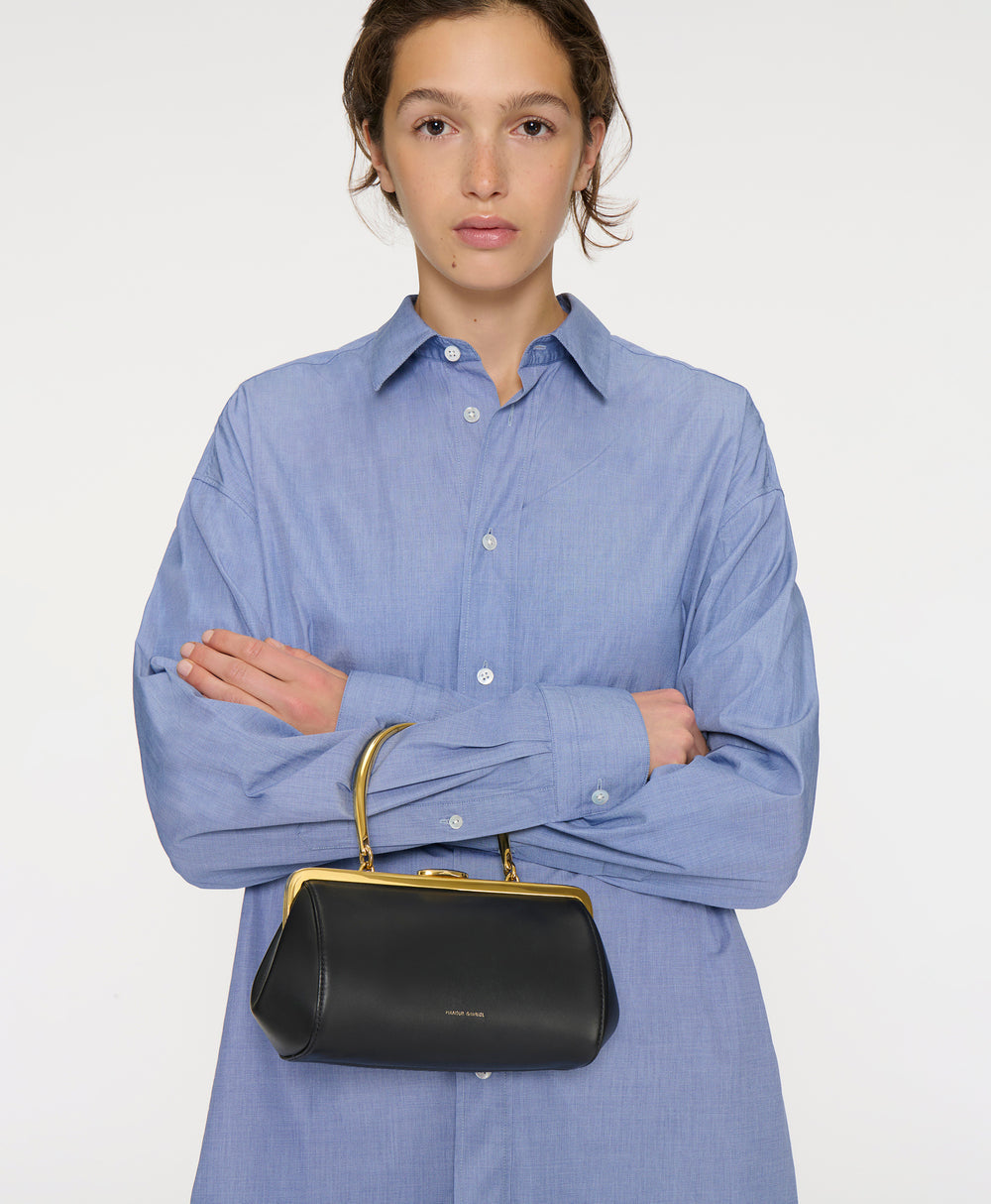 Front view of Pina Evening Bag in black showcasing gold metal frame and sculptural handle held by model against white background