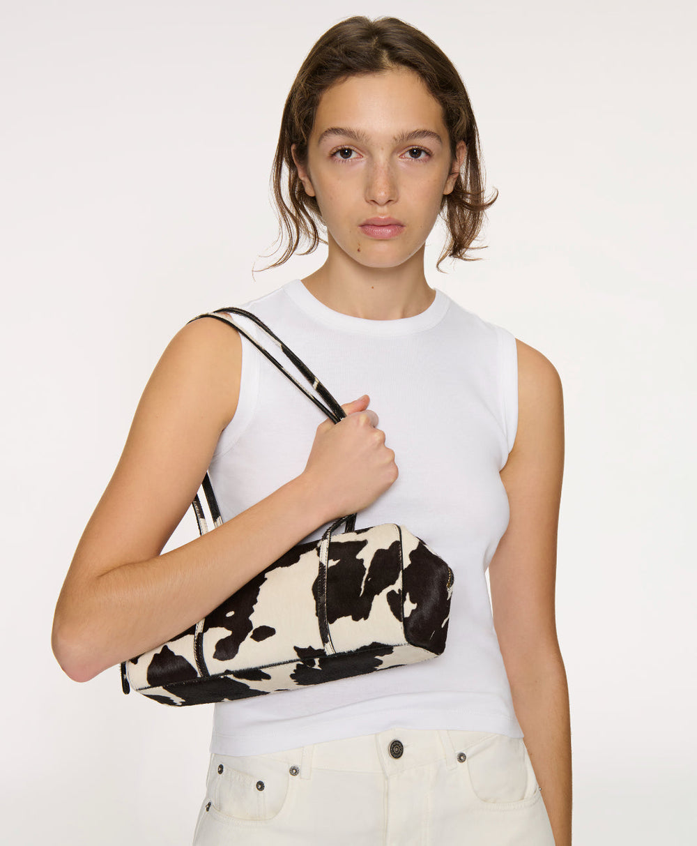 Three quarter view of Filo Bag in Printed Ponyhair showcasing cow print haircalf exterior and thin double shoulder straps on a model