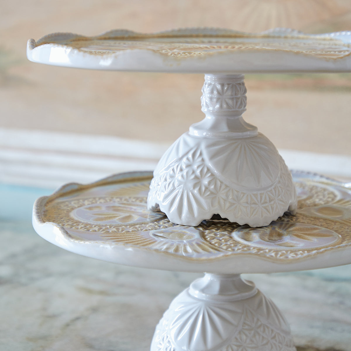 Side view of Costa Nova Cristal footed plate in Nacar showcasing elevated silhouette and crystal-inspired pattern with blurred background