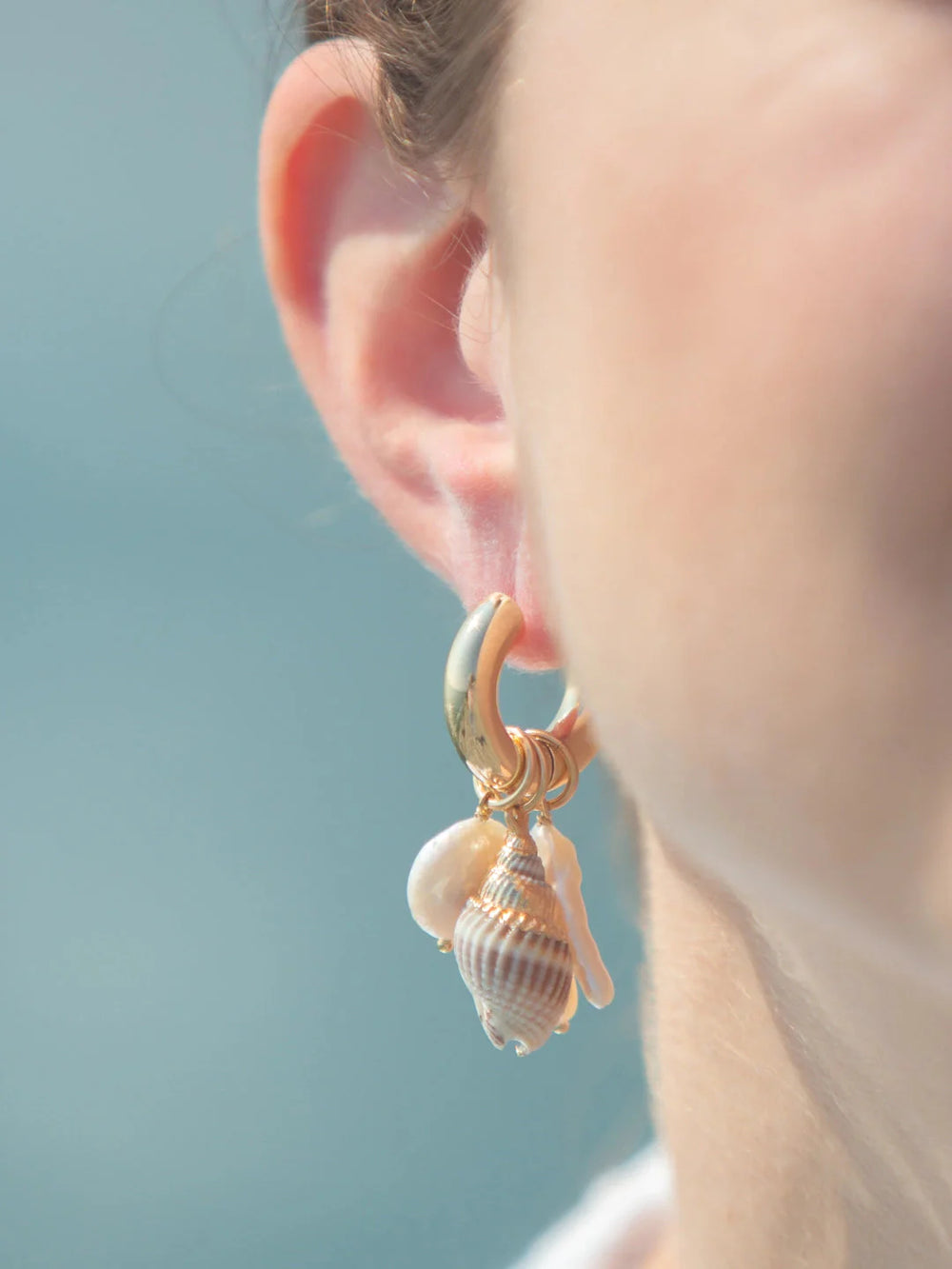 Close-up of Talia earrings on ear showing gold-plated hoop with dangling freshwater pearls and shell charms