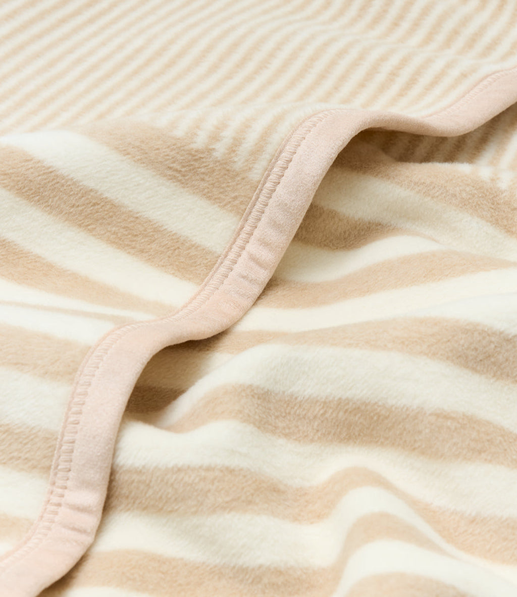 Beige and cream striped blanket with pink binding edge, folded to show texture and stitching detail.