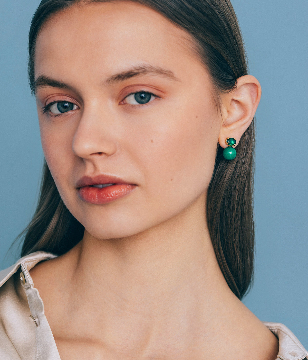 Close-up view of Sabine Studs in Green showcasing green stone bead and crystal worn by a model against a blue background