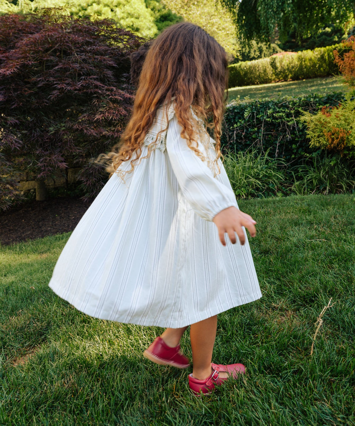 Back view of Sara Dress in Sage Chevron Stripe showcasing the embroidered yoke and collar in a garden