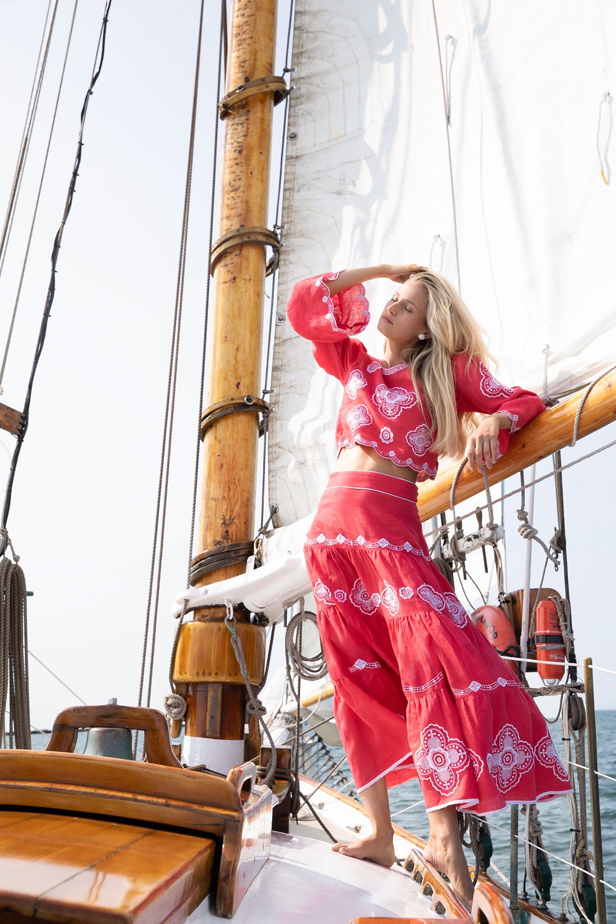 Three-quarter view of Scarlet Willow Top on model showcasing red linen, white clover embroidery and scalloped trim on a sailboat