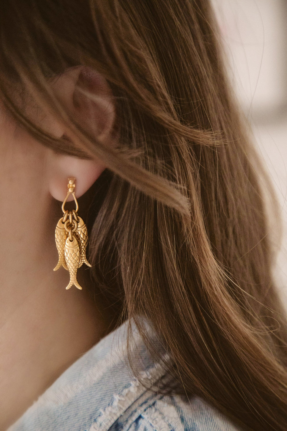 Side close-up of School Of Fish earrings showing three antique gold-plated fish charms dangling from a stud on a model’s ear