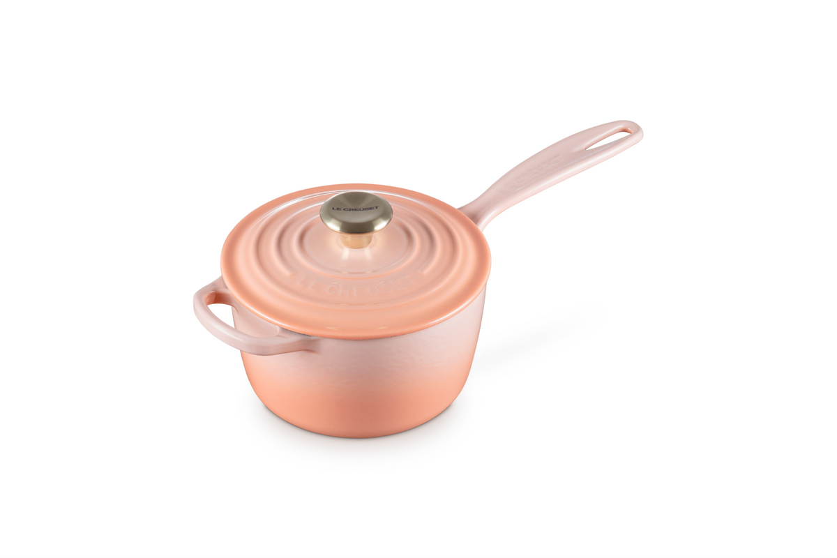 Front three-quarter view of Signature Saucepan in Peche showcasing its lid and two handles on a white background