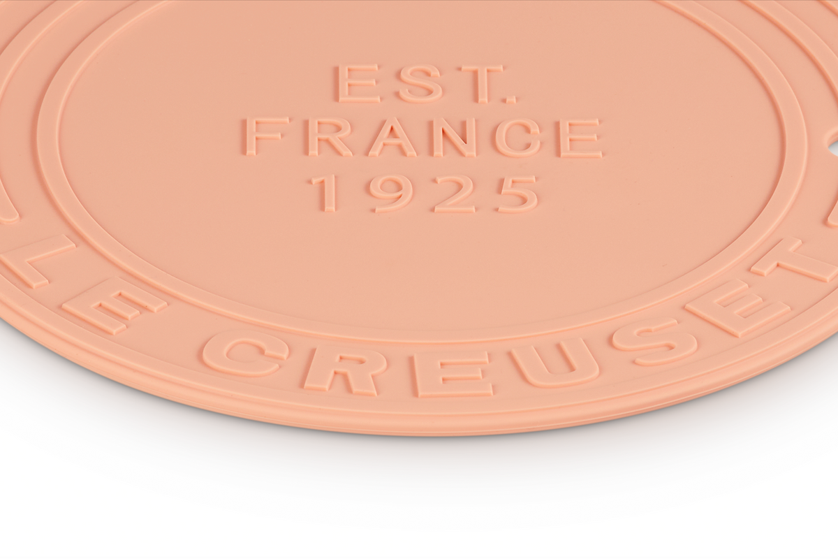 Close-up of Silicone Trivet in Peche showcasing raised Le Creuset and Est France 1925 lettering on white background