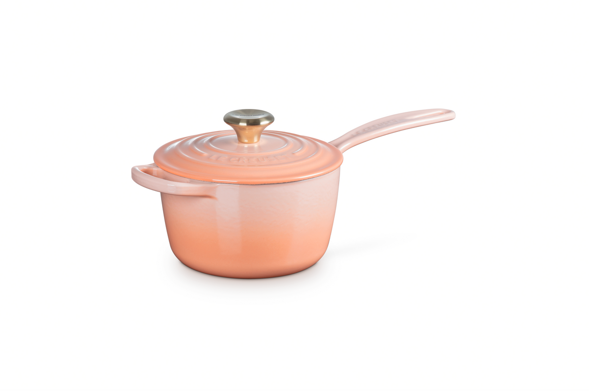Three-quarter view of Signature Saucepan in Peche showcasing its lid and extended handles with a white background