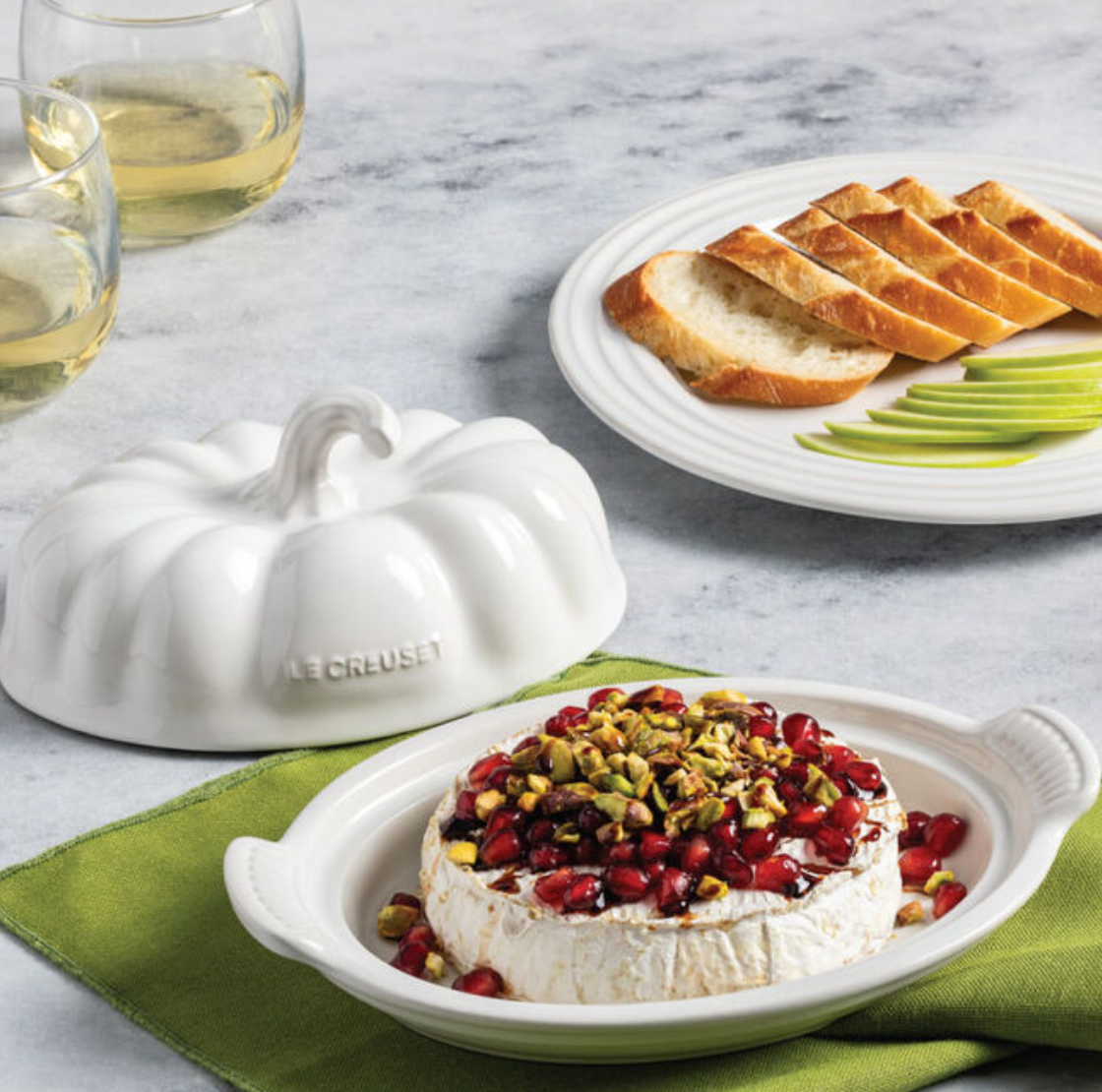 Front view of white pumpkin butter dish with lid removed, showing baked brie topped with pomegranate and pistachios