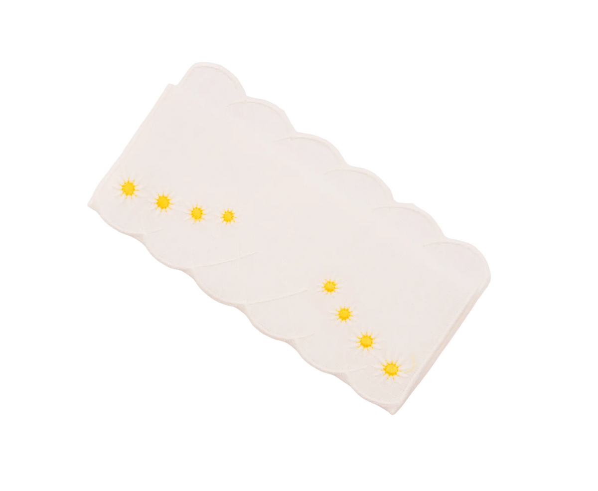 Angled flat lay of Daisy Aperitivo cocktail napkins showing scalloped edges and yellow embroidered daisies on white background