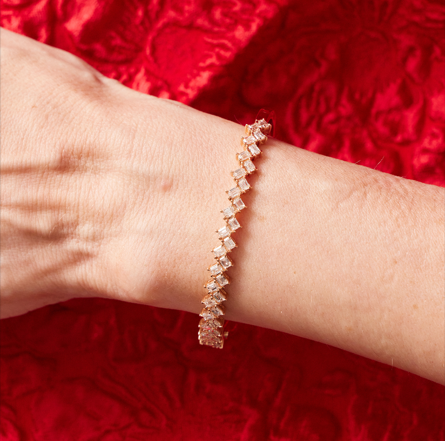 The Zig Zag Motif Emerald Cut Diamond Bangle with VS clarity diamonds is shown on a wrist, set against a textured red fabric background.