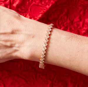 The Zig Zag Motif Emerald Cut Diamond Bangle with VS clarity diamonds is shown on a wrist, set against a textured red fabric background.