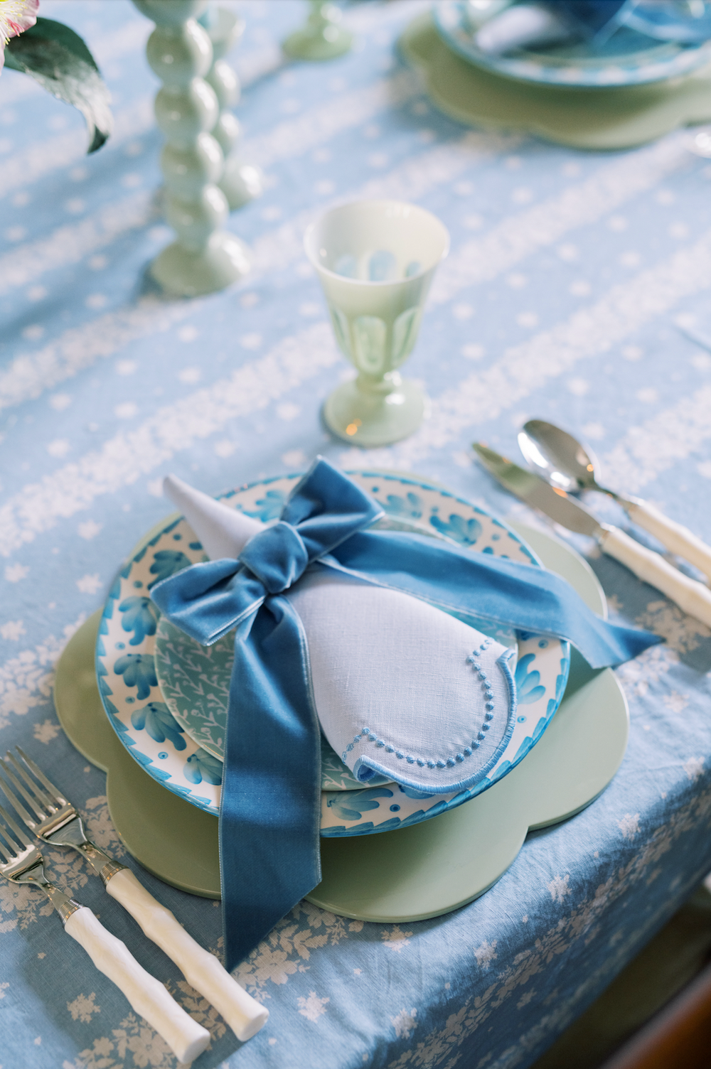 Close-up of blue-dotted white linen napkin on scalloped placemat, napkin tied with blue velvet bow on blue tablecloth