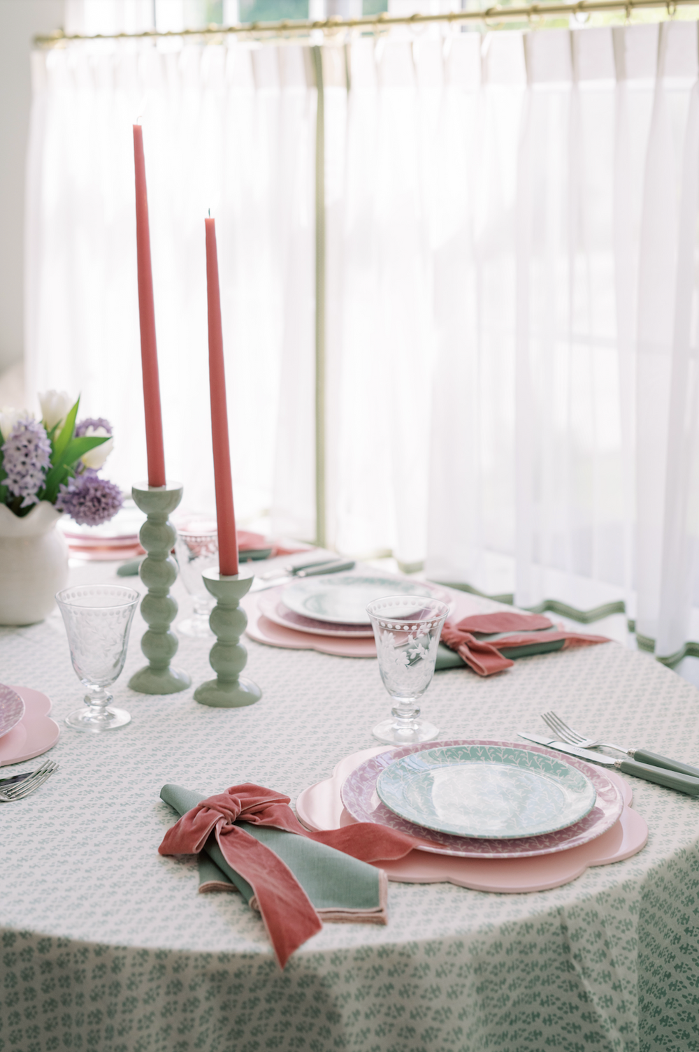Pink velvet napkin bows tied around green cloth napkins on a pastel table setting with scalloped plates and taper candles