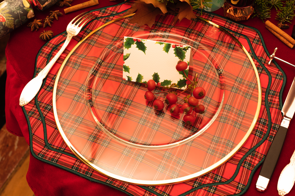 Overhead view of Stucco Red Tartan napkin and placemat set showcasing tartan plaid, scalloped edges, and green trim on red linen with charger