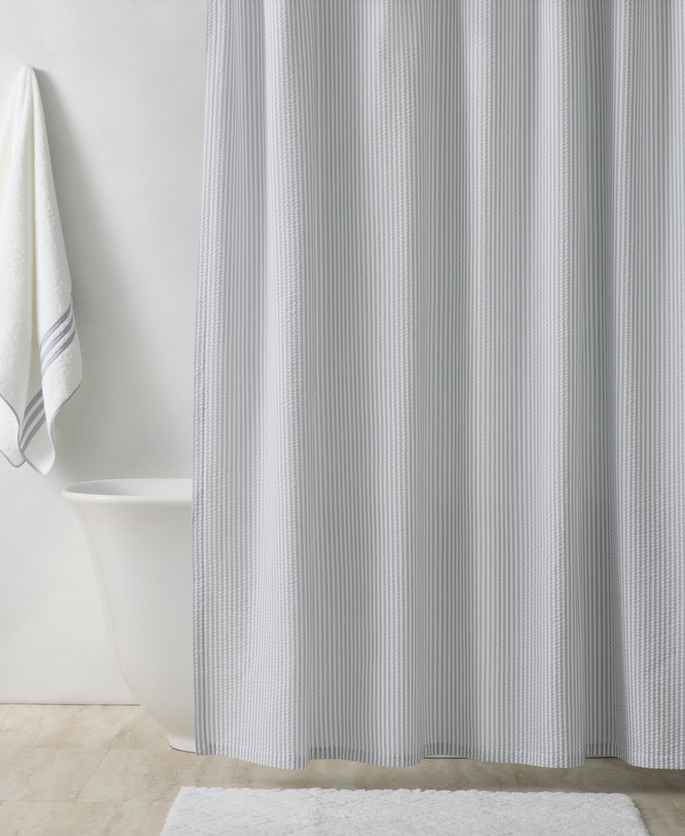 Front view of Matteo Shower Curtain showcasing blue seersucker stripes with freestanding tub and towel