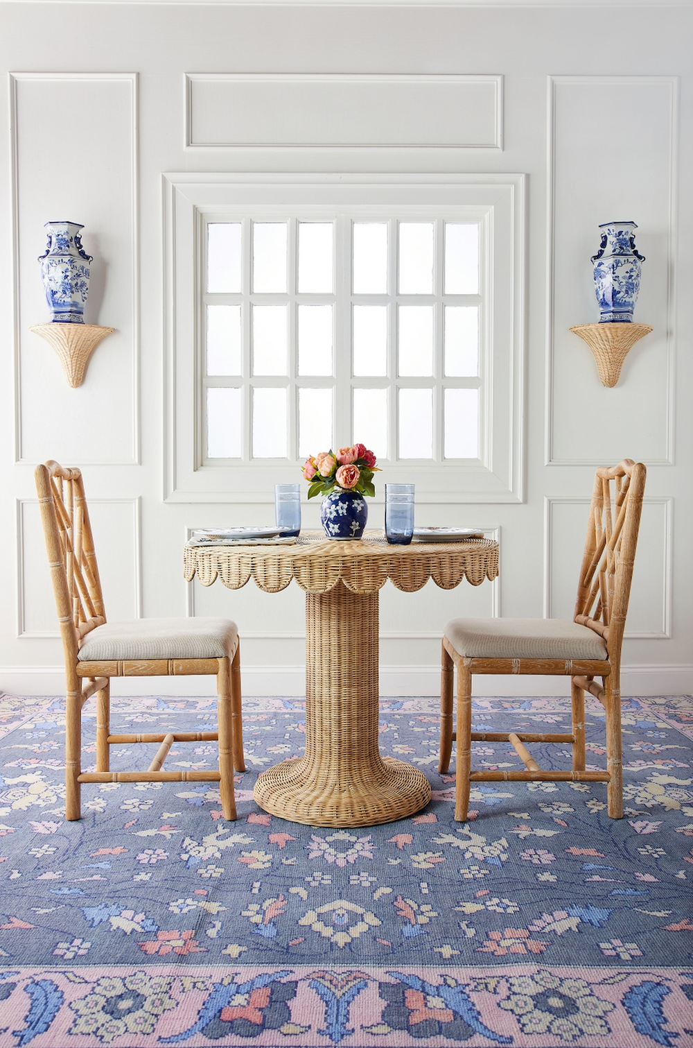 Front view of Coco Bistro table showing wicker scalloped edge and pedestal base, with two rattan chairs and floral centerpiece
