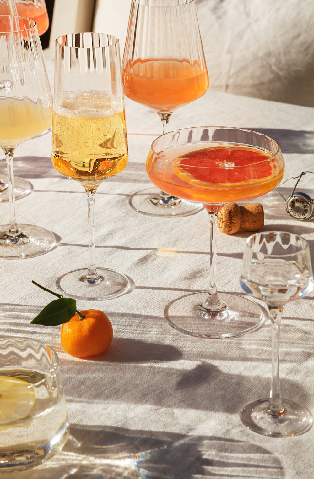 Bernadotte crystal wine glasses arranged on a sunlit linen table with cocktails, grapefruit slice, and a clementine