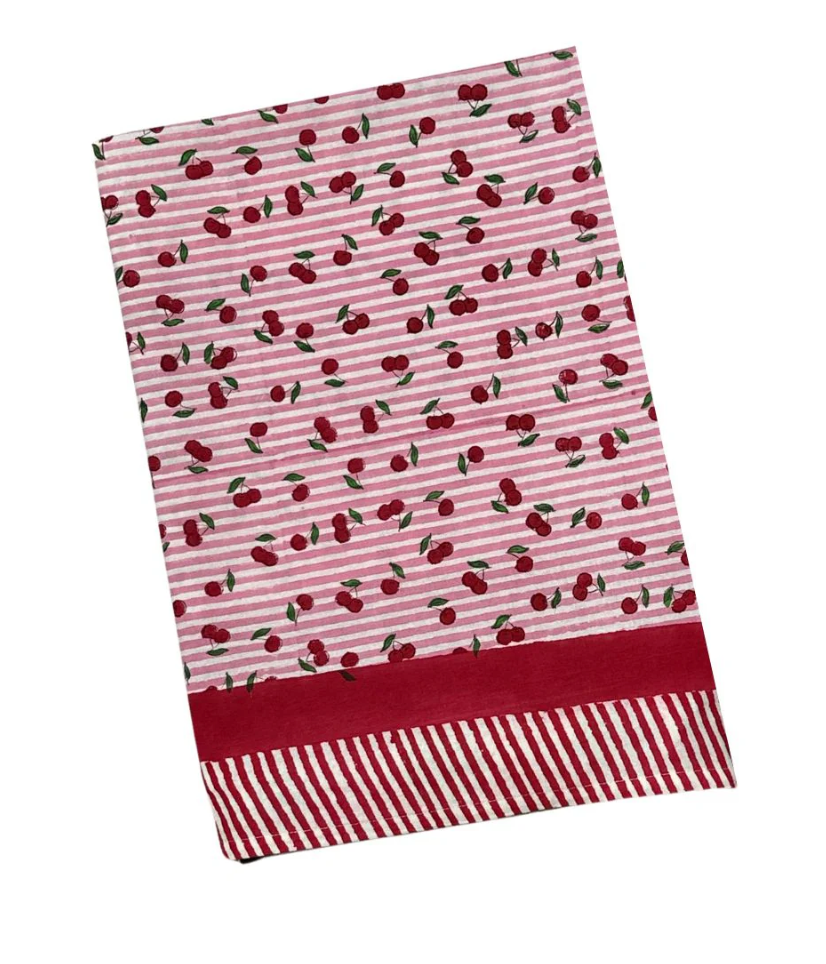 Angled flat lay of tablecloth in Cherry with pink-and-white stripes, scattered red cherries, and red striped border on white