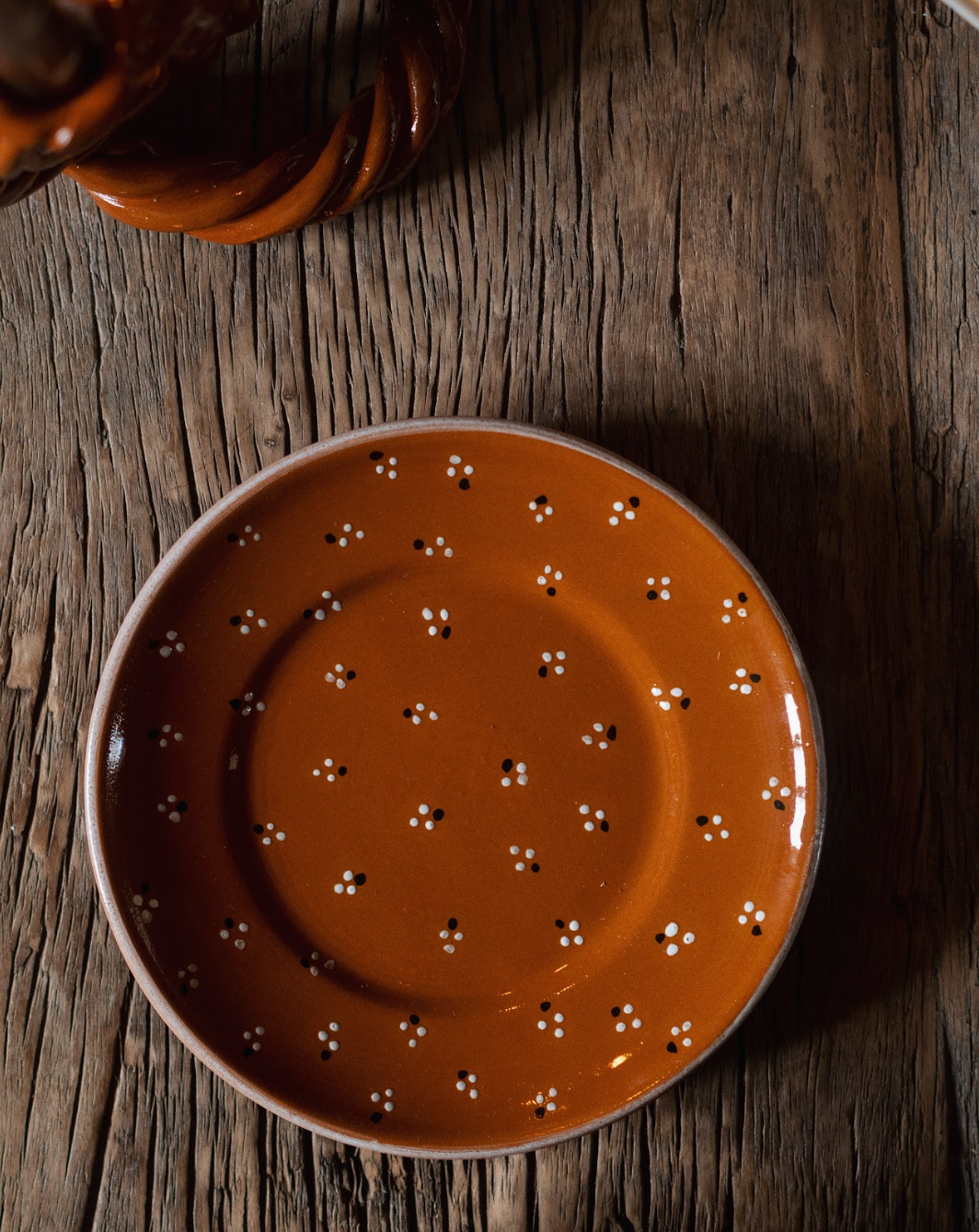 Top view of Dotty side plate showcasing terracotta glaze with white and black dot clusters on a rustic wood table