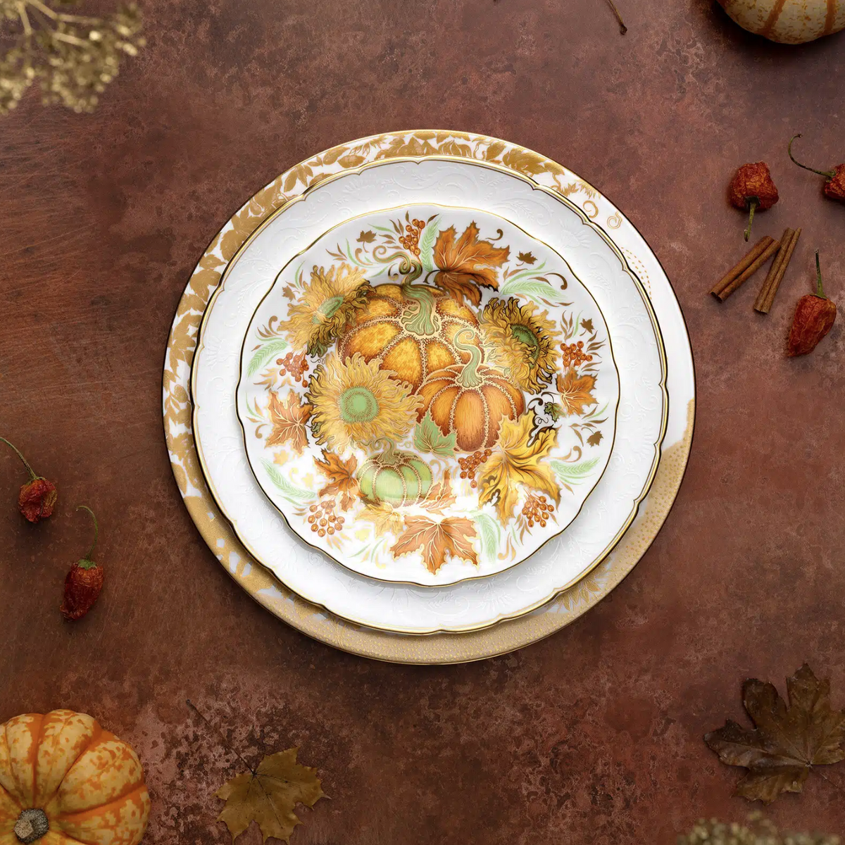 Top view of Holiday Accent plate showcasing autumn pumpkin and sunflower motif with 22 carat gold trim on a brown tabletop