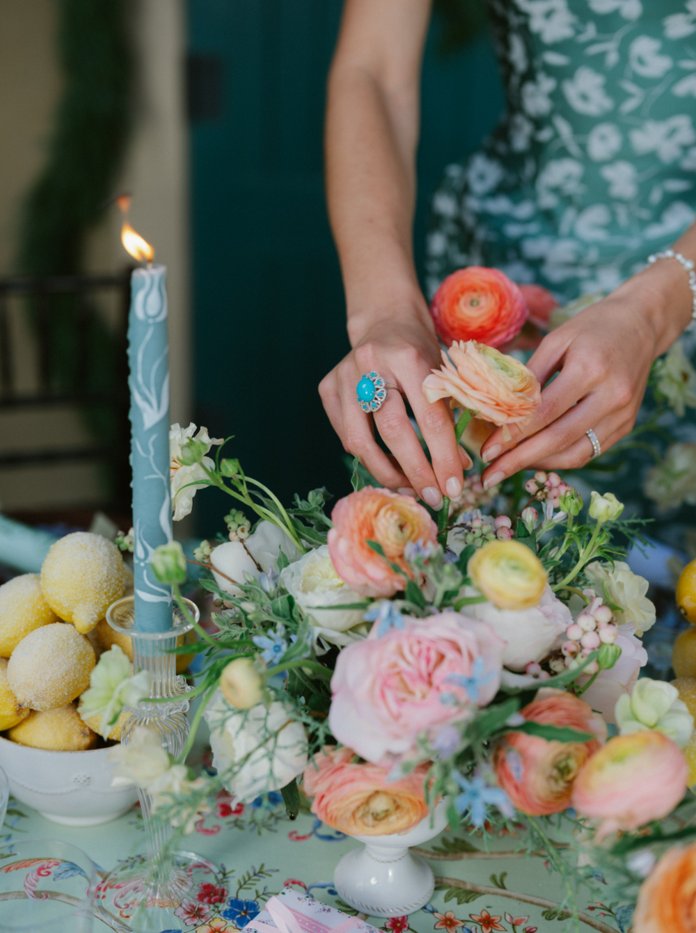 Hands arranging pastel ranunculus and roses on a table while wearing a turquoise cabochon ring with a diamond halo