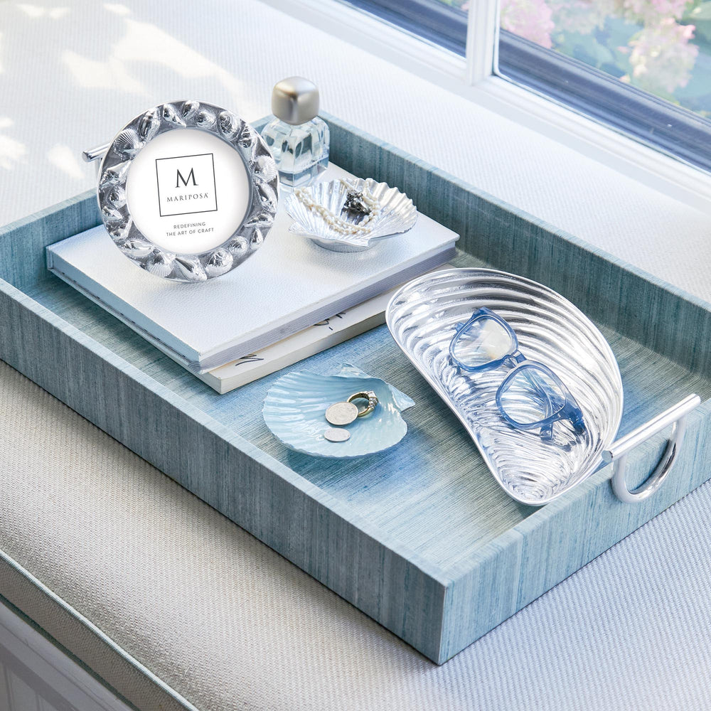 Angled view of dusty blue scallop trinket dish showing seashell shape and glossy finish on a blue textured tray