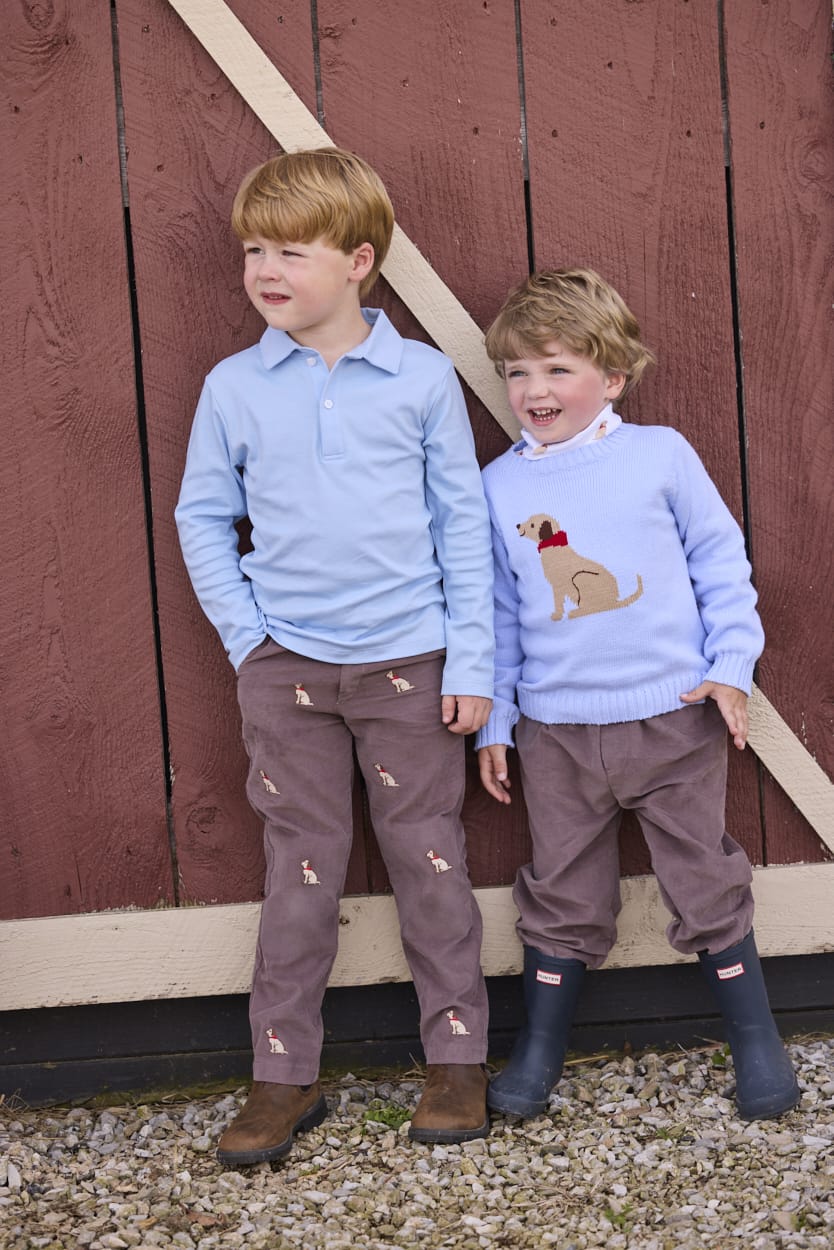 Little English traditional children's clothing.  Classic long sleeve light blue polo and chocolate brown corduroy pants with seated lab embroidery for boys.  Light blue crew neck intarsia sweater with seated lab motif layered over lab printed turtleneck and paired with chocolate brown corduroy banded pants.