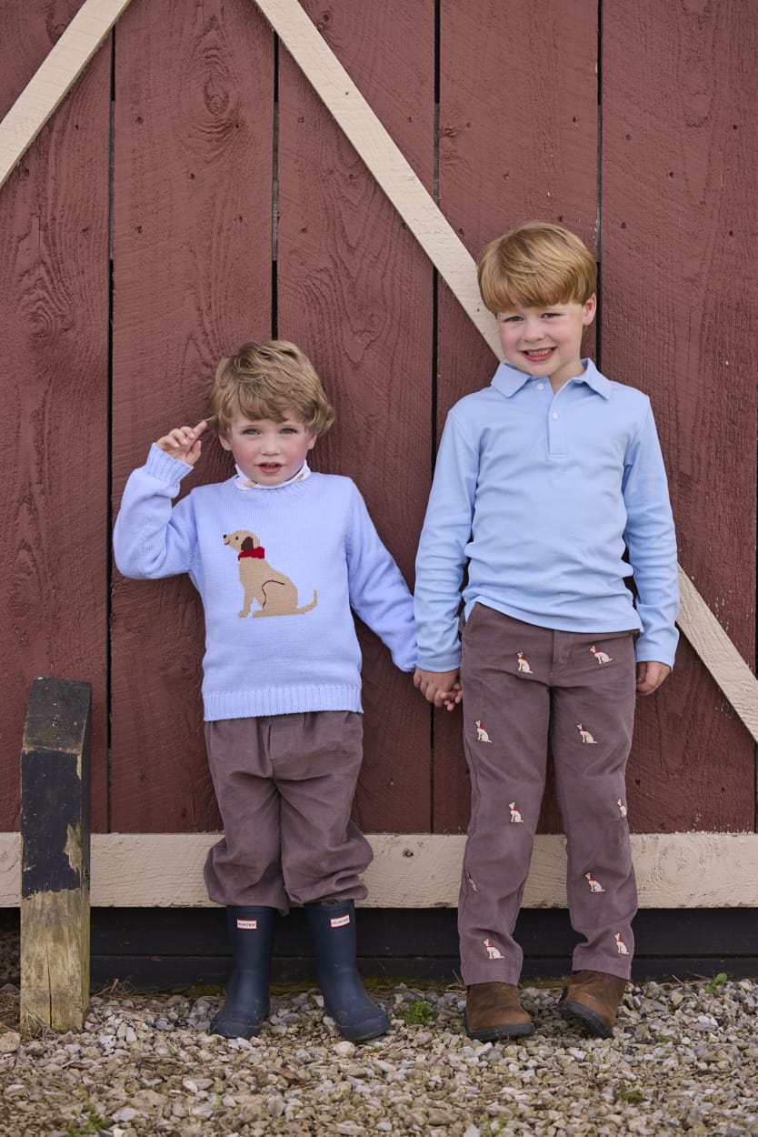 Little English traditional children's clothing.  Classic long sleeve light blue polo and chocolate brown corduroy pants with seated lab embroidery for boys.  Light blue crew neck intarsia sweater with seated lab motif layered over lab printed turtleneck and paired with chocolate brown corduroy banded pants.