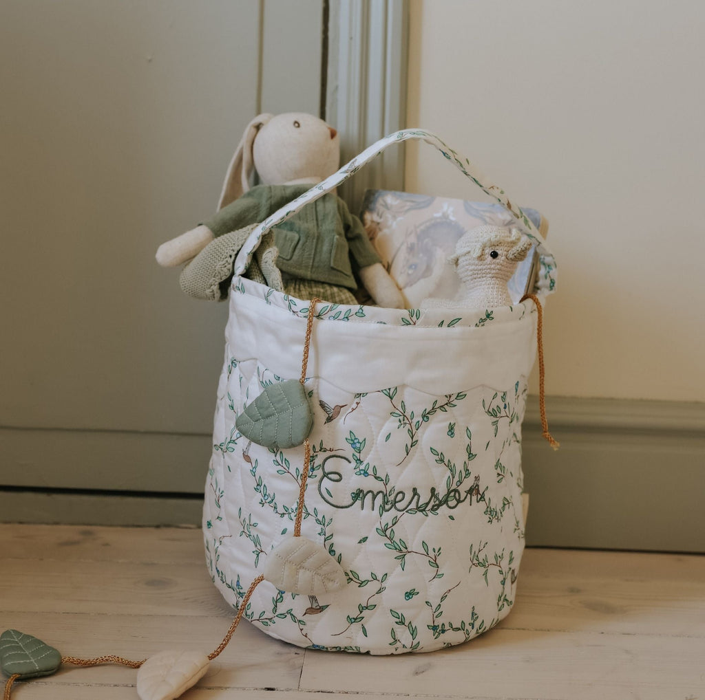 Vine-patterned toy storage basket with stuffed animals on a wooden floor.