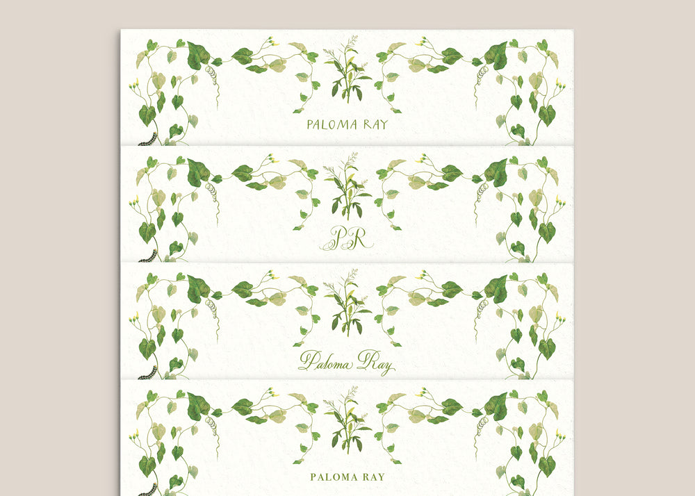Flat lay of Selva stationery strips showing green watercolor vine borders and personalized names on textured cream paper