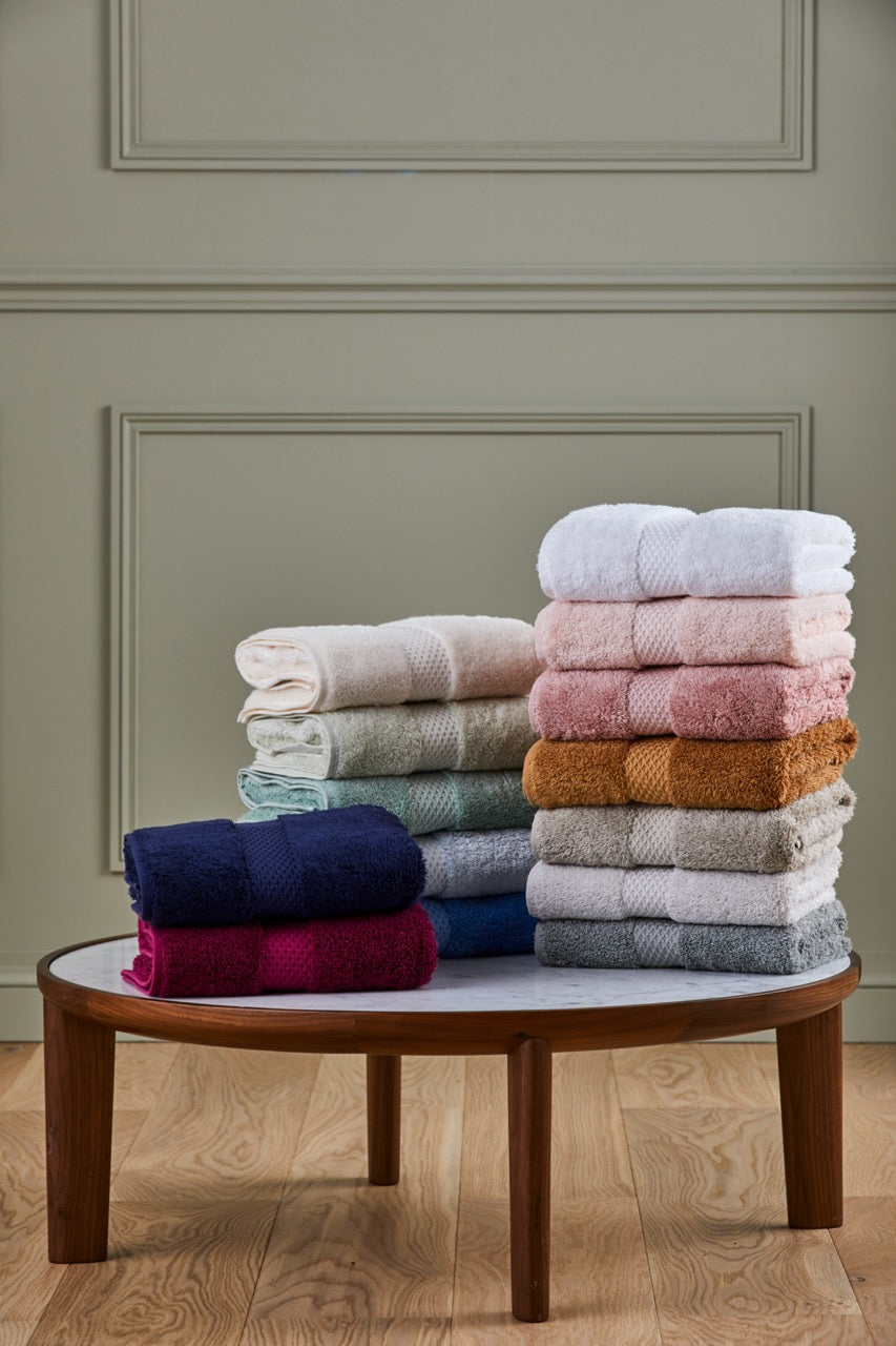 Etoile bath sheets stacked to show star-pattern decorative band and assorted colors on a round table against a paneled wall