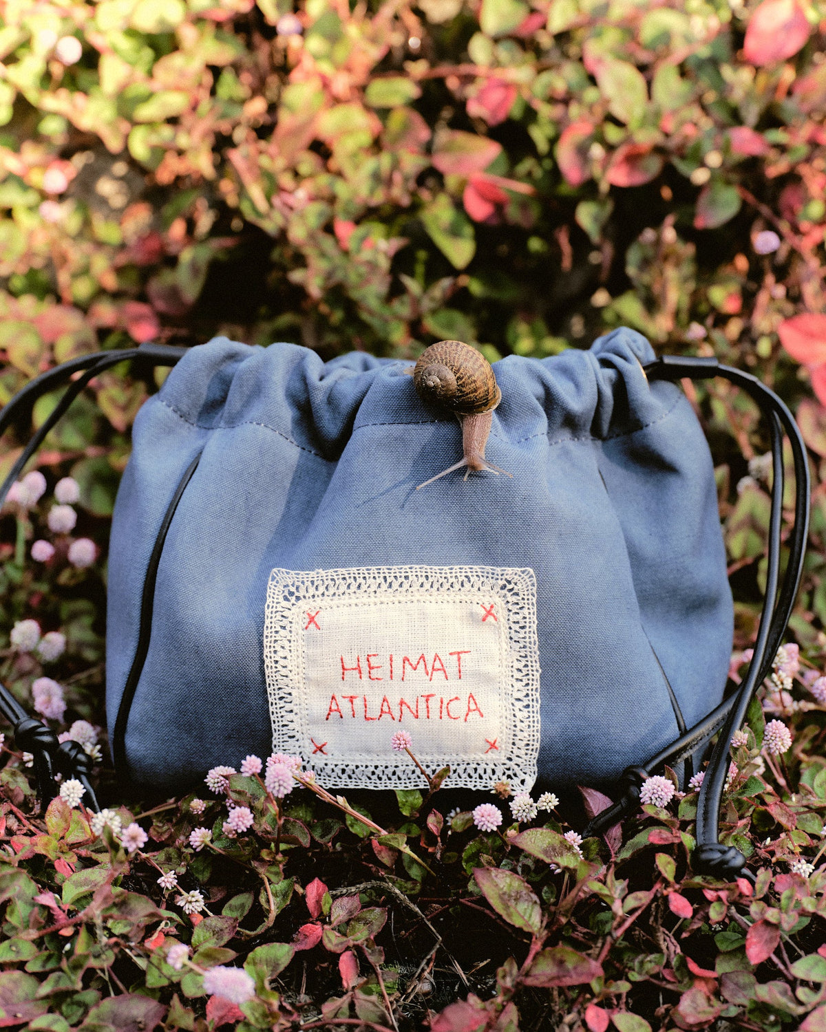 Front close-up of the Camarinas Pouch in Denim showcasing its handmade bobbin lace linen label and leather drawstrings