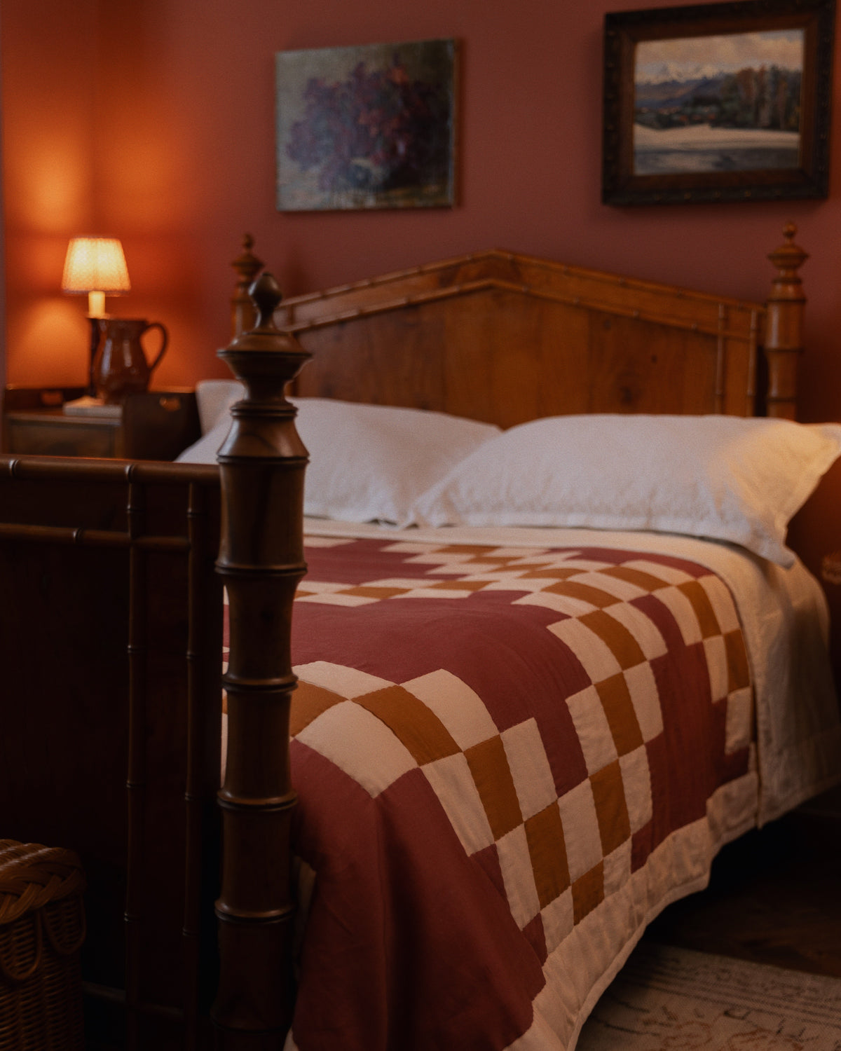 Three-quarter view of Prairie Quilt showing hand-stitched terracotta and cream checkerboard patchwork on a wooden bed in a warm bedroom