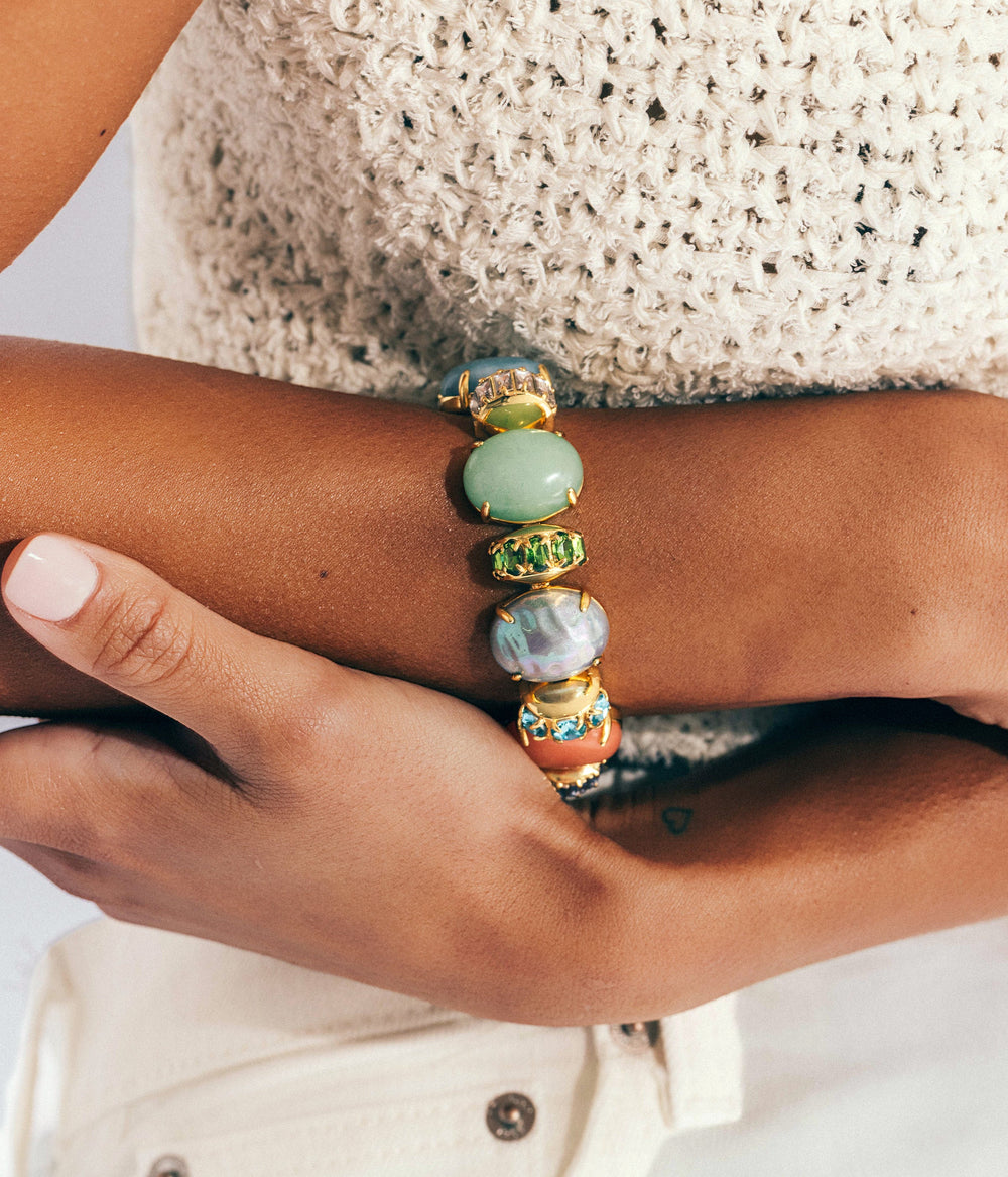 Close up of Sheridan Bracelet on a model’s wrist showing multicolored cabochons and faceted crystal accents in a gold setting against a cream knit top