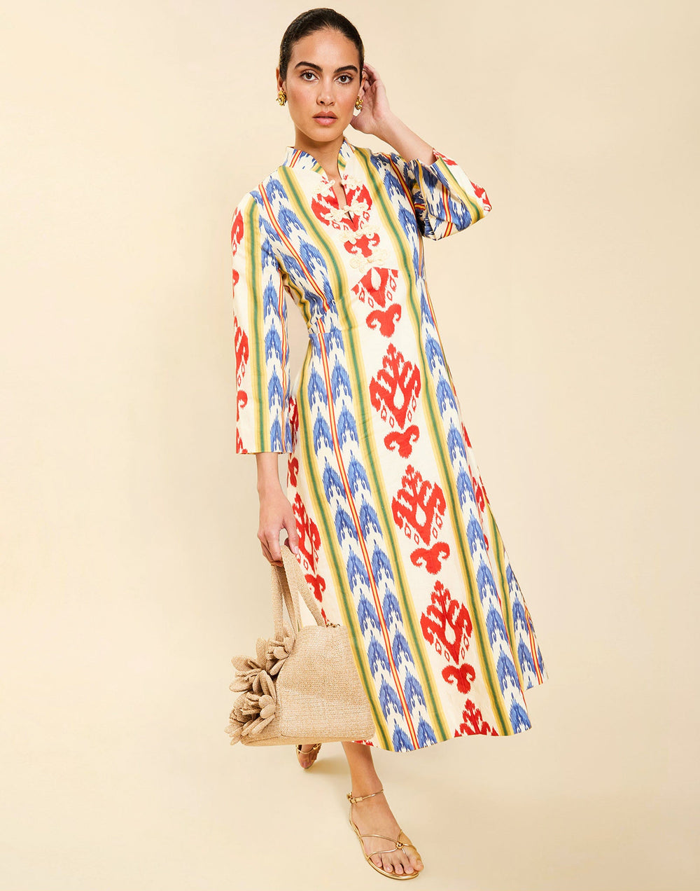 Woman wearing the Mestiza Shoshi Midi Dress in Ikat Sunrise print, featuring a fitted bodice, A-line midi skirt, mandarin collar, functional frog tie closures, side seam pockets, and linen fabrication.