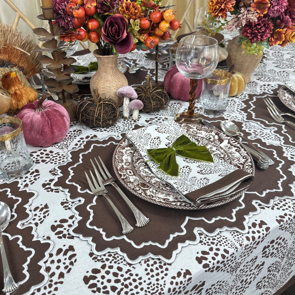 Decorative table setting with pumpkins, flowers, and cutlery on a patterned tablecloth. Luxury embroidered placemat and block print napkin
