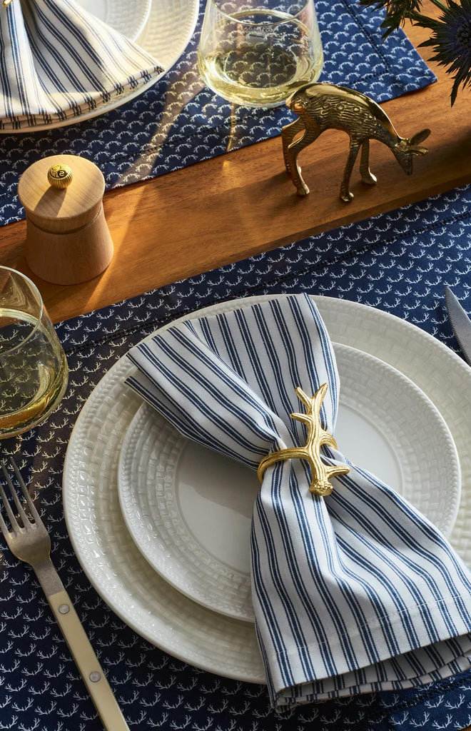 Close-up of folded twill napkin with navy ticking stripes and gold antler napkin ring on navy patterned tablecloth